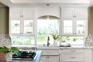 Open concept kitchen - large traditional u-shaped dark wood floor open concept kitchen idea in San Diego with a farmhouse sink, shaker cabinets, white cabinets, wood countertops, gray backsplash, paneled appliances and an island