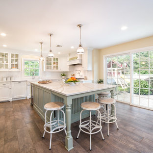 Design ideas for a large country u-shaped kitchen/diner in New York with a belfast sink, white cabinets, engineered stone countertops, white splashback, metro tiled splashback, stainless steel appliances, porcelain flooring, an island, brown floors, white worktops and shaker cabinets.
