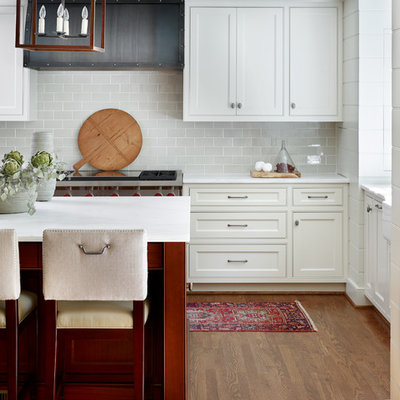 Mid-sized transitional u-shaped medium tone wood floor and brown floor enclosed kitchen photo in Atlanta with beaded inset cabinets, white cabinets, gray backsplash, an island, a farmhouse sink, subway tile backsplash, stainless steel appliances and marble countertops