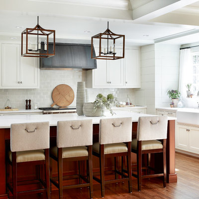 Mid-sized transitional u-shaped medium tone wood floor and brown floor kitchen photo in Atlanta with an island, a farmhouse sink, beaded inset cabinets, white cabinets, gray backsplash, subway tile backsplash, stainless steel appliances and marble countertops