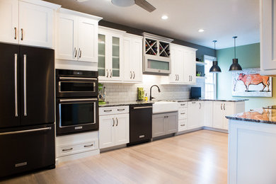Example of a large transitional galley light wood floor and beige floor enclosed kitchen design in Indianapolis with a farmhouse sink, shaker cabinets, white cabinets, granite countertops, white backsplash, subway tile backsplash and black appliances