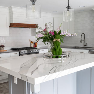 This is an example of a mid-sized country l-shaped eat-in kitchen in Atlanta with an undermount sink, shaker cabinets, white cabinets, quartz benchtops, white splashback, ceramic splashback, stainless steel appliances, vinyl floors, with island, grey floor and white benchtop.