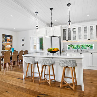 Photo of a mid-sized transitional l-shaped open plan kitchen in Sydney with white cabinets, marble benchtops, multi-coloured splashback, marble splashback, medium hardwood floors, multiple islands, brown floor, white benchtop, stainless steel appliances, a drop-in sink and shaker cabinets.