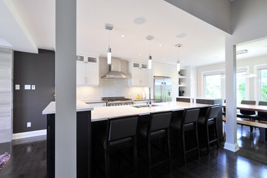 Example of a large trendy galley dark wood floor open concept kitchen design in Ottawa with an undermount sink, shaker cabinets, white cabinets, quartz countertops, white backsplash, subway tile backsplash, stainless steel appliances and an island