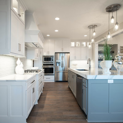 Open concept kitchen - craftsman l-shaped medium tone wood floor and brown floor open concept kitchen idea in Kansas City with a drop-in sink, white cabinets, white backsplash, stainless steel appliances, an island and white countertops