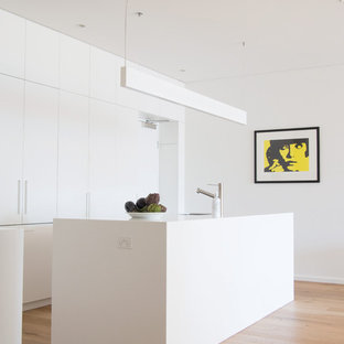 Inspiration for a modern l-shaped kitchen with flat-panel cabinets, white cabinets, medium hardwood floors, with island, brown floor, white benchtop and panelled appliances.