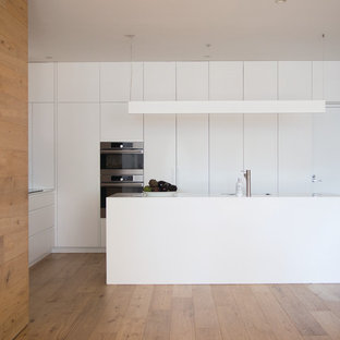 Modern l-shaped kitchen with flat-panel cabinets, white cabinets, stainless steel appliances, medium hardwood floors, with island, beige floor and white benchtop.