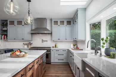 Example of a large transitional u-shaped medium tone wood floor and brown floor kitchen design in San Francisco with a farmhouse sink, shaker cabinets, quartz countertops, white backsplash, brick backsplash, stainless steel appliances, white countertops, gray cabinets and an island