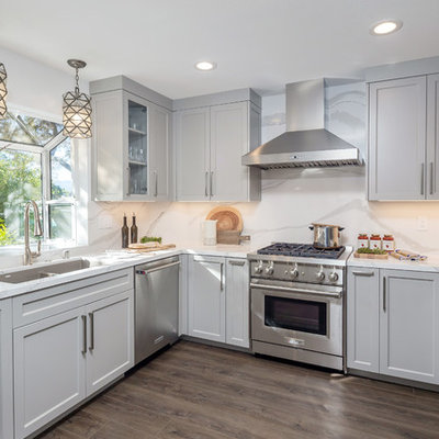 Example of a mid-sized transitional u-shaped medium tone wood floor and brown floor kitchen design in San Francisco with quartz countertops, white backsplash, stainless steel appliances, no island, white countertops, a double-bowl sink, shaker cabinets and gray cabinets