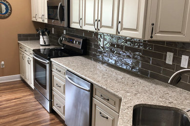 Mid-sized elegant l-shaped brown floor eat-in kitchen photo in Other with a double-bowl sink, raised-panel cabinets, beige cabinets, quartz countertops, brown backsplash, ceramic backsplash, stainless steel appliances and beige countertops