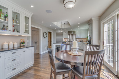 Eat-in kitchen - mid-sized transitional l-shaped brown floor and tray ceiling eat-in kitchen idea in Manchester with an undermount sink, shaker cabinets, white cabinets, stainless steel appliances and an island