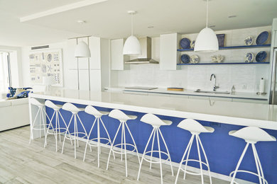 Inspiration for a mid-sized contemporary galley porcelain tile and white floor open concept kitchen remodel in Miami with a single-bowl sink, flat-panel cabinets, white cabinets, quartzite countertops, white backsplash, porcelain backsplash, stainless steel appliances, an island and white countertops