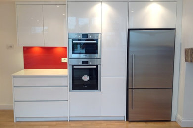Modern open plan kitchen in London with white cabinets, red splashback and stainless steel appliances.