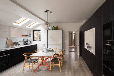 Design ideas for a medium sized contemporary galley kitchen/diner in Gloucestershire with a submerged sink, flat-panel cabinets, black cabinets, composite countertops, white splashback, stone slab splashback, black appliances, no island, white worktops and beige floors.