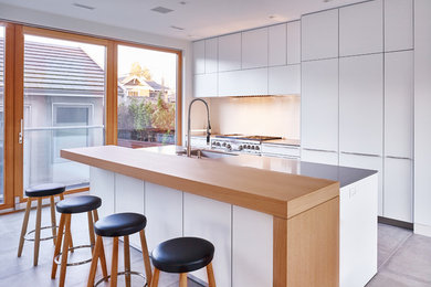 Modern inredning av ett mellanstort linjärt kök och matrum, med en undermonterad diskho, släta luckor, vita skåp, vitt stänkskydd, rostfria vitvaror, klinkergolv i porslin och en köksö
