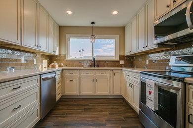 Example of a small classic u-shaped dark wood floor and brown floor kitchen design in Phoenix with an undermount sink, recessed-panel cabinets, beige cabinets, brown backsplash, glass tile backsplash, stainless steel appliances, no island and beige countertops
