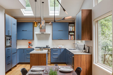 Example of a large minimalist u-shaped light wood floor and brown floor open concept kitchen design in San Francisco with an undermount sink, flat-panel cabinets, blue cabinets, solid surface countertops, white backsplash, stone slab backsplash, stainless steel appliances and an island