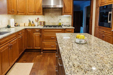 Exempel på ett avskilt, stort klassiskt u-kök, med en undermonterad diskho, luckor med upphöjd panel, skåp i mellenmörkt trä, granitbänkskiva, beige stänkskydd, stänkskydd i stenkakel, rostfria vitvaror, mörkt trägolv, en köksö och brunt golv