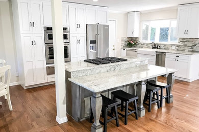 Mid-sized elegant l-shaped light wood floor and brown floor eat-in kitchen photo in Sacramento with a farmhouse sink, shaker cabinets, white cabinets, granite countertops, green backsplash, stone tile backsplash, stainless steel appliances and an island