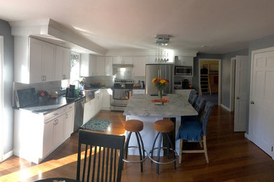 Large cottage l-shaped bamboo floor and brown floor eat-in kitchen photo in Boston with a farmhouse sink, shaker cabinets, white cabinets, marble countertops, white backsplash, ceramic backsplash, stainless steel appliances, an island and multicolored countertops