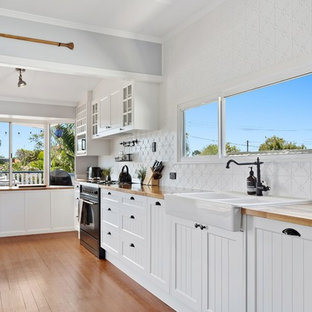 Inspiration for a transitional single-wall kitchen in Gold Coast - Tweed with a farmhouse sink, shaker cabinets, white cabinets, white splashback, black appliances and medium hardwood floors.