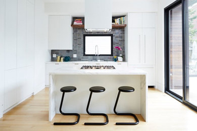This is an example of a modern l-shaped kitchen/diner in Toronto with a submerged sink, flat-panel cabinets, white cabinets, marble worktops, grey splashback, porcelain splashback, integrated appliances, light hardwood flooring and an island.