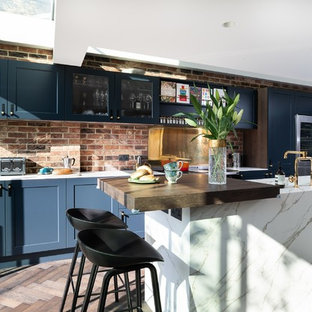 Design ideas for a mid-sized modern galley eat-in kitchen in Other with an integrated sink, shaker cabinets, blue cabinets, quartz benchtops, metallic splashback, metal splashback, black appliances, painted wood floors, with island, brown floor and white benchtop.