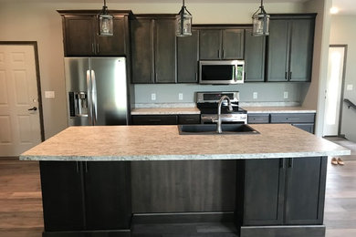 Photo of a large traditional galley open plan kitchen in Cedar Rapids with a double-bowl sink, shaker cabinets, dark wood cabinets, laminate countertops, stainless steel appliances, an island and grey worktops.