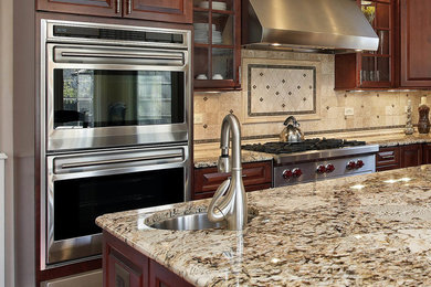 Kitchen - mid-sized traditional l-shaped kitchen idea in Denver with a farmhouse sink, dark wood cabinets, granite countertops, beige backsplash, travertine backsplash, stainless steel appliances and an island