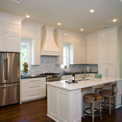 Example of a mid-sized classic galley enclosed kitchen design in New Orleans with recessed-panel cabinets, stainless steel appliances, stone tile backsplash, white cabinets, white backsplash and an island