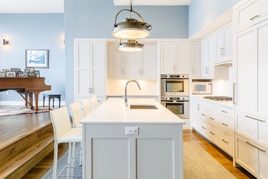 Example of a large classic l-shaped dark wood floor eat-in kitchen design in New York with an undermount sink, shaker cabinets, white cabinets, quartz countertops, white backsplash, ceramic backsplash, paneled appliances and an island