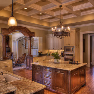 Inspiration pour une grand cuisine traditionnelle en U fermée avec un électroménager en acier inoxydable, un plan de travail en granite, un évier encastré, un placard avec porte à panneau surélevé, des portes de placard beiges, une crédence beige, une crédence en travertin, un sol en bois brun et un îlot central.