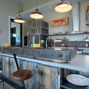 Idée de décoration pour une grand cuisine ouverte parallèle urbaine avec un évier 2 bacs, des portes de placard en bois vieilli, un plan de travail en verre recyclé, une crédence métallisée, un électroménager en acier inoxydable, béton au sol et un îlot central.