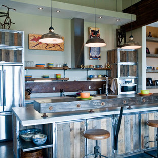Large industrial galley open plan kitchen in Other with distressed cabinets, stainless steel appliances, with island, a double-bowl sink, recycled glass benchtops, metallic splashback, concrete floors and open cabinets.