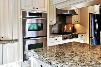 タンパにある広いトラディショナルスタイルのおしゃれなアイランドキッチン (レイズドパネル扉のキャビネット、白いキャビネット、御影石カウンター、シルバーの調理設備) の写真