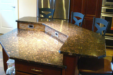 Modelo de cocina de tamaño medio con puertas de armario de madera en tonos medios, encimera de granito, electrodomésticos de acero inoxidable, suelo de pizarra y una isla