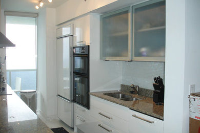 Enclosed kitchen - mid-sized modern galley ceramic tile enclosed kitchen idea in Miami with a double-bowl sink, flat-panel cabinets, white cabinets, granite countertops, white backsplash, porcelain backsplash, paneled appliances and no island