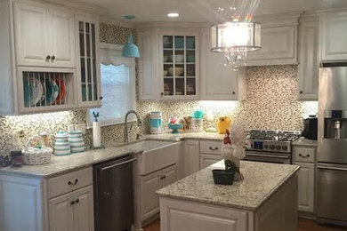Example of a mid-sized transitional l-shaped medium tone wood floor and brown floor kitchen design in New Orleans with a farmhouse sink, raised-panel cabinets, white cabinets, granite countertops, multicolored backsplash, mosaic tile backsplash, stainless steel appliances and an island