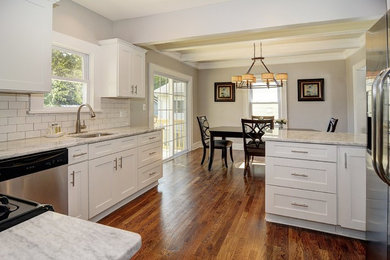 Large u-shaped medium tone wood floor eat-in kitchen photo in New York with an undermount sink, shaker cabinets, white cabinets, marble countertops, white backsplash, subway tile backsplash, stainless steel appliances and no island