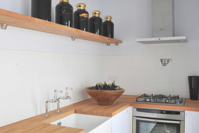 ロンドンにある小さなモダンスタイルのおしゃれなキッチン (エプロンフロントシンク、フラットパネル扉のキャビネット、グレーのキャビネット、木材カウンター、白いキッチンパネル、磁器タイルのキッチンパネル、シルバーの調理設備、クッションフロア、アイランドなし) の写真