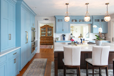 Example of a mid-sized beach style medium tone wood floor enclosed kitchen design in Boston with beaded inset cabinets, marble countertops, white backsplash, porcelain backsplash, an island, a farmhouse sink, blue cabinets, stainless steel appliances and white countertops