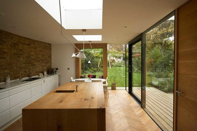 Medium sized contemporary single-wall enclosed kitchen in London with a double-bowl sink, flat-panel cabinets, white cabinets, wood worktops, light hardwood flooring, an island and beige floors.