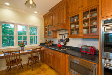 Inspiration for a mid-sized craftsman galley medium tone wood floor and brown floor enclosed kitchen remodel in Other with a farmhouse sink, recessed-panel cabinets, medium tone wood cabinets, soapstone countertops, white backsplash, ceramic backsplash, stainless steel appliances, no island and black countertops
