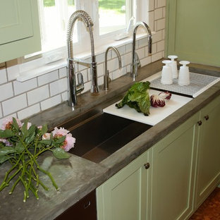 This is an example of a mid-sized country l-shaped separate kitchen in St Louis with a farmhouse sink, shaker cabinets, green cabinets, concrete benchtops, white splashback, subway tile splashback, black appliances, cork floors, no island and brown floor.