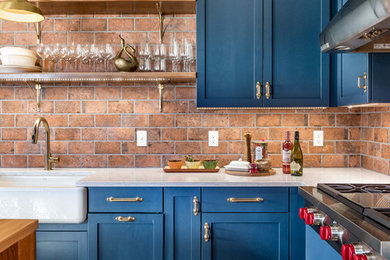 Modelo de cocina campestre con fregadero sobremueble, armarios estilo shaker, puertas de armario azules, encimera de cuarcita, suelo de madera en tonos medios y una isla