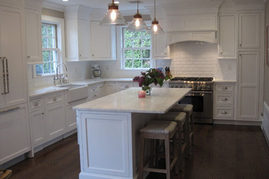 Example of a transitional l-shaped medium tone wood floor eat-in kitchen design in New York with a farmhouse sink, recessed-panel cabinets, white cabinets, marble countertops, white backsplash, subway tile backsplash, stainless steel appliances and an island