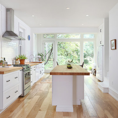 Example of a large transitional galley medium tone wood floor and brown floor eat-in kitchen design in Philadelphia with a farmhouse sink, shaker cabinets, white cabinets, wood countertops, white backsplash, subway tile backsplash, stainless steel appliances and an island