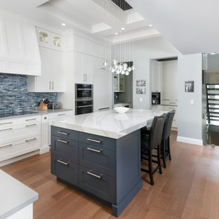 Imagen de cocina comedor en L, clásica renovada, grande, con puertas de armario blancas, salpicadero azul, electrodomésticos de acero inoxidable, una isla, armarios con paneles lisos, encimera de cuarzo compacto, suelo de madera clara, suelo beige y encimeras blancas