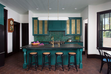 Пример оригинального дизайна: кухня в стиле фьюжн с обеденным столом, врезной мойкой, зелеными фасадами, зеленым фартуком, черной техникой, островом, коричневым полом и окном