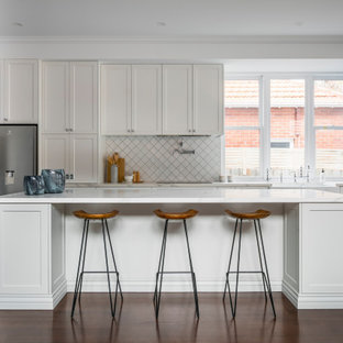Inspiration for a mid-sized transitional galley kitchen in Melbourne with a farmhouse sink, shaker cabinets, white cabinets, quartz benchtops, stainless steel appliances, dark hardwood floors, with island, brown floor and white benchtop.